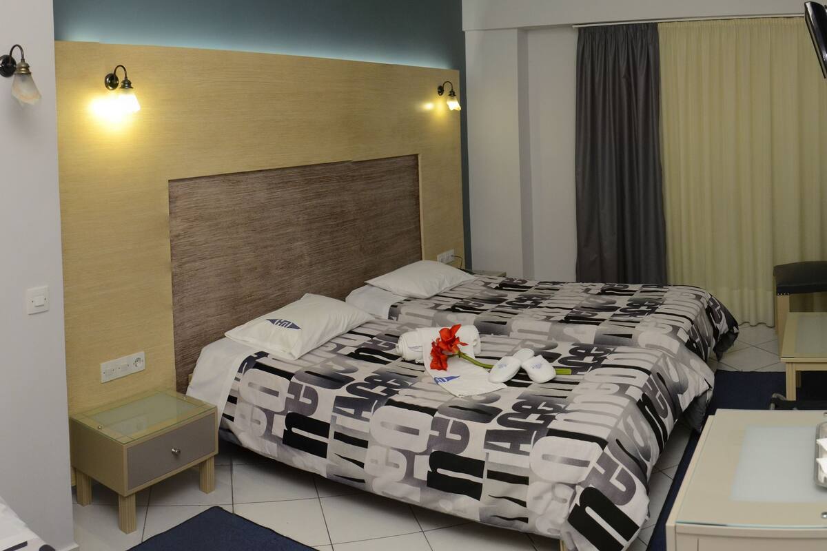 A hotel room with a bed, bedside table, and a small table with a glass.