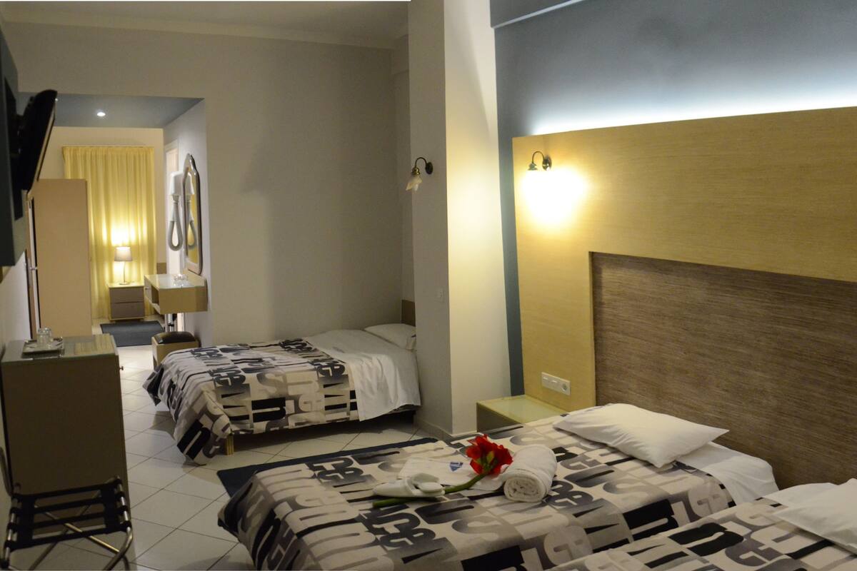 A hotel room with two beds, a desk, a chair, a lamp, and a television.