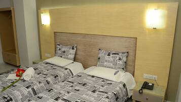 Una habitación de hotel con cabecera de madera, dos camas con ropa de cama estampada con motivos de periódico, una mesita de noche con teléfono e iluminación de pared.