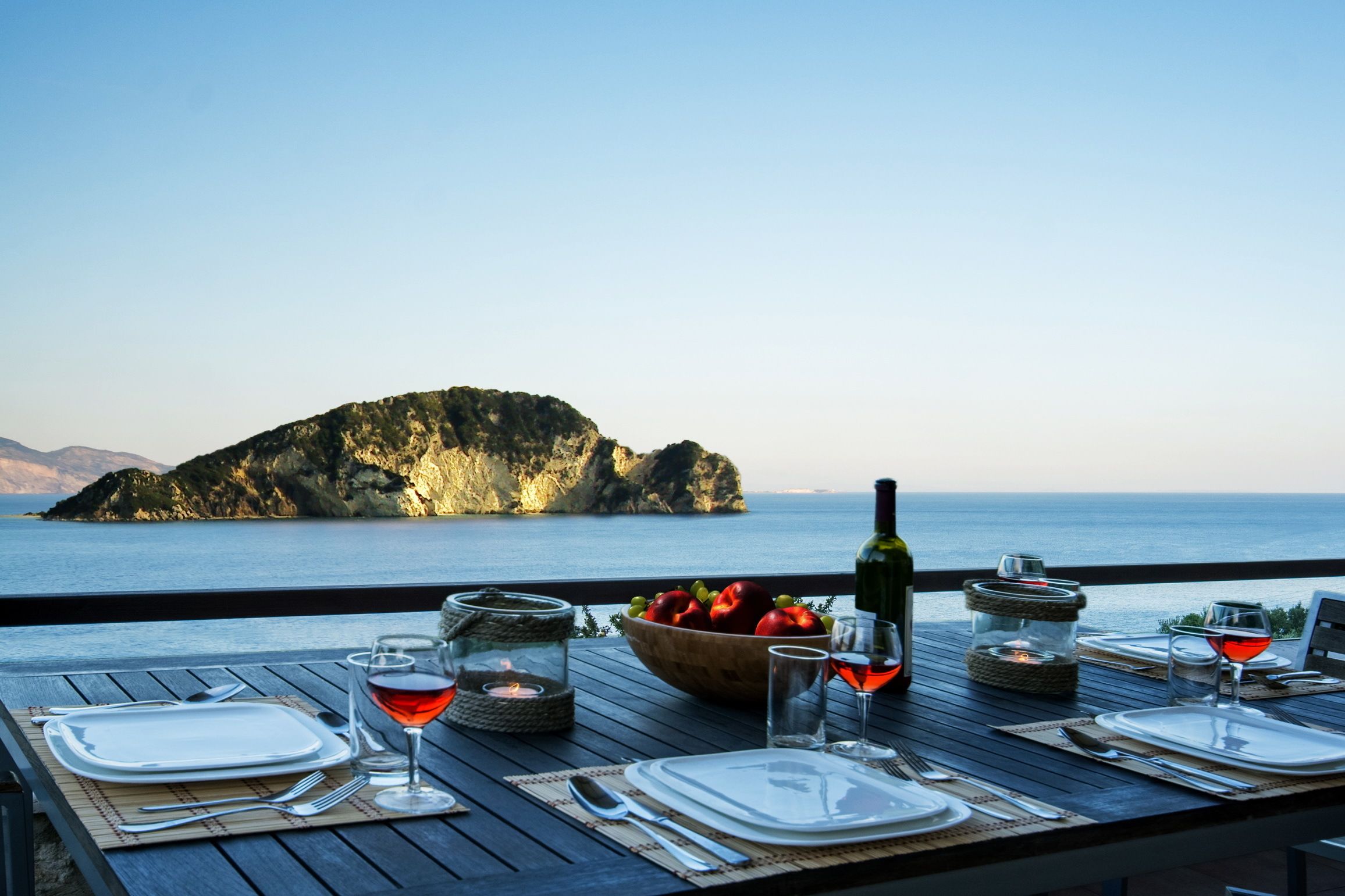 Een eettafel gedekt voor twee met uitzicht op zee en een verre eiland.