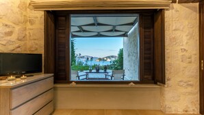 A room with a large window overlooking a patio area with a table and chairs, stone walls, and a flat-screen TV on a wooden cabinet.