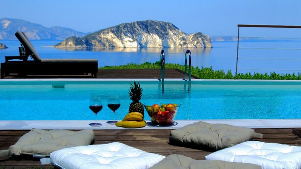 A poolside area with lounge chairs, a fruit bowl, and glasses of wine.