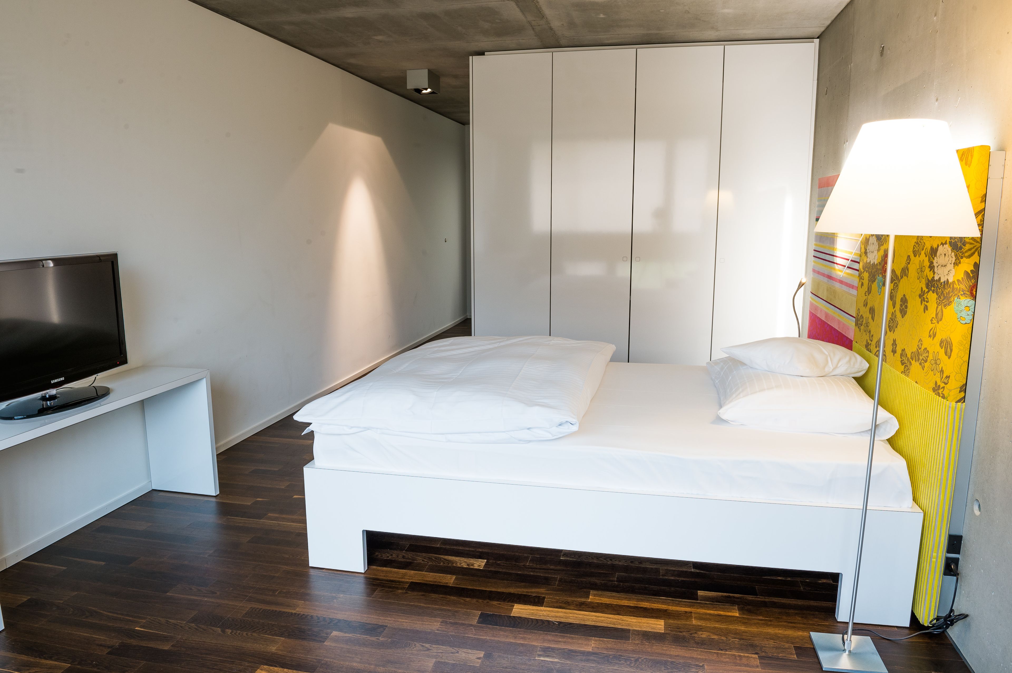 A modern bedroom with a bed, a TV on a stand, and a lamp.