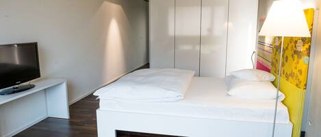 A modern bedroom with a bed, a TV on a stand, and a lamp.