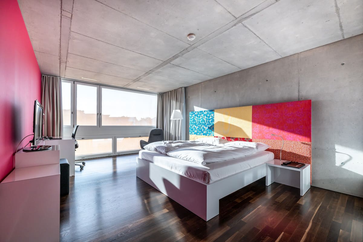 A modern bedroom with a large bed, a bedside table, a desk, and a chair.