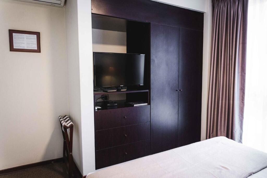 A hotel room with a bed, a dark wooden wardrobe with a television, and a framed notice on the wall.