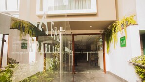 A hotel entrance with a glass door, a sign indicating the name 'LA PAZ', and a green sign with 'AH' on the wall. - La Paz Apart Hotel (Lima)