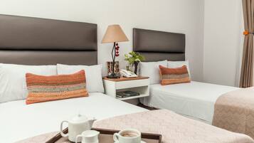 A hotel room with two beds, a bedside table with a lamp, a phone, a plant, and a tray with a teapot, cups, and a book.