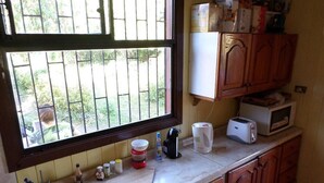A kitchen with a window, wooden cabinets, a microwave, and various kitchen items on the counter. - Hostal Emalafquen (Pucon)