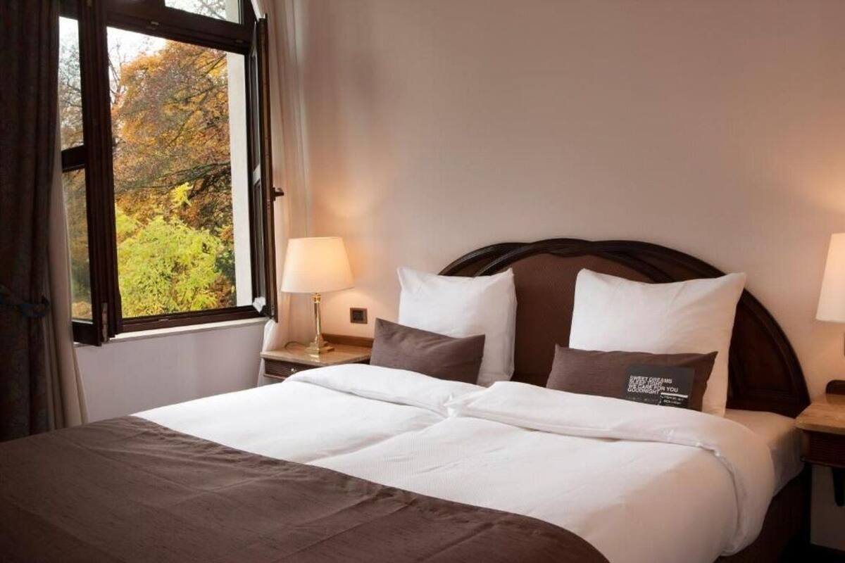 A neatly made bed with white and brown bedding, a wooden headboard, and a nightstand with a lamp.