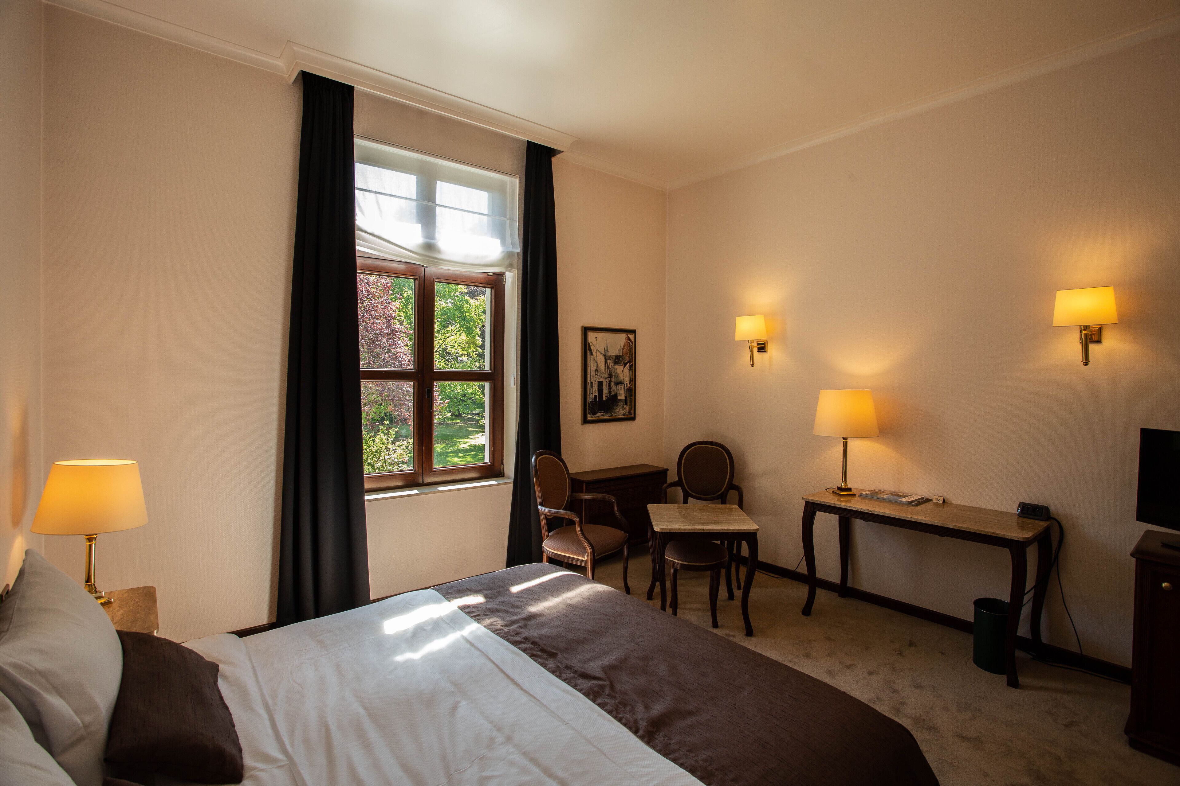 A hotel room with a bed, desk, chair, and two wall-mounted lamps.