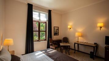 A hotel room with a bed, desk, chair, and two wall-mounted lamps.