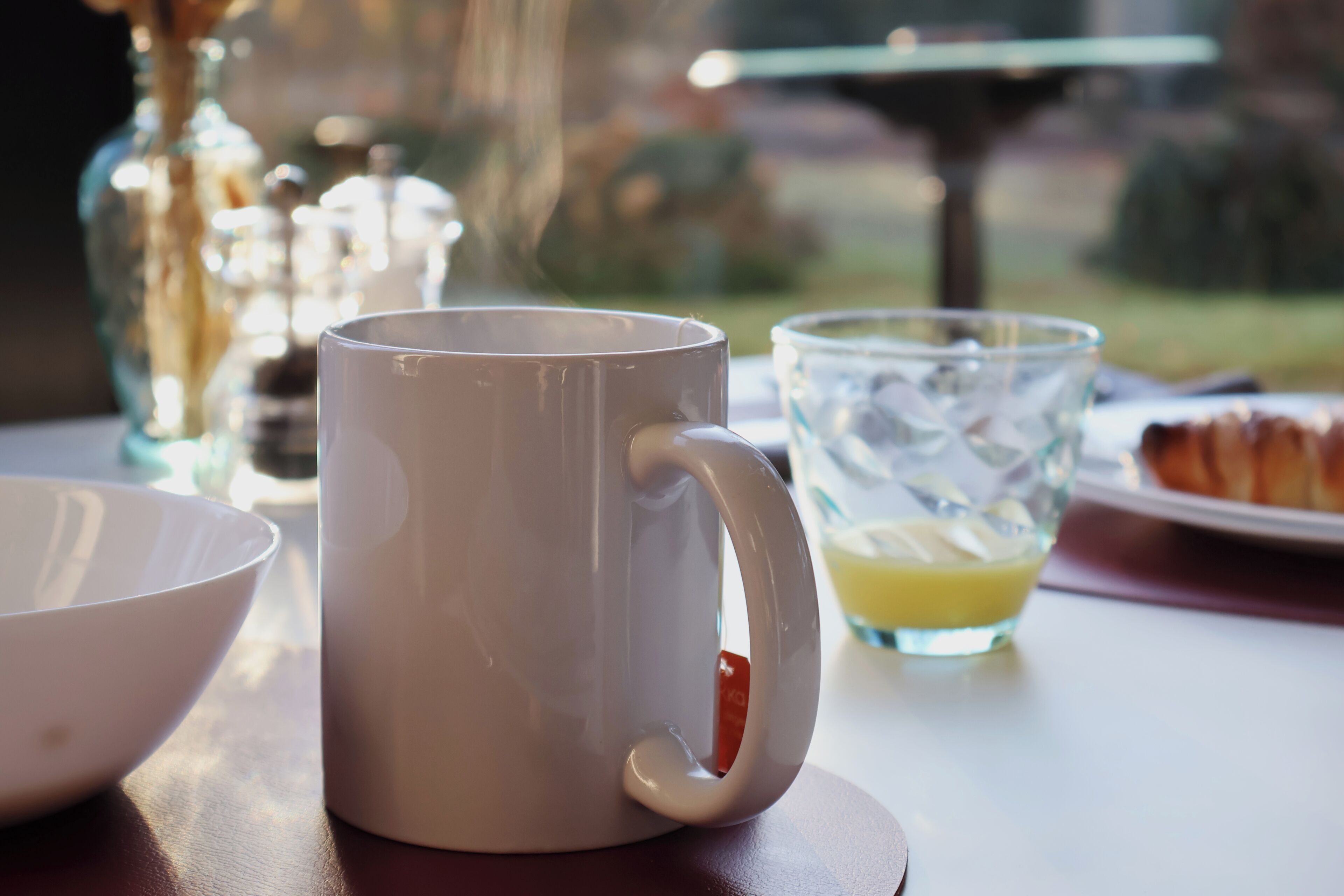 A white mug with a handle on a table, a glass with a yellow liquid, and a white bowl.
