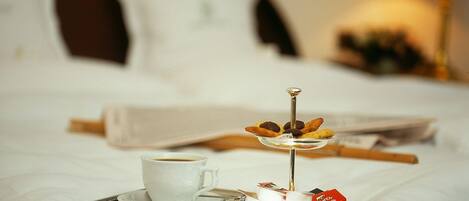 A neatly made bed with a tray containing a cup of coffee, a small plate with pastries, and a decorative item.