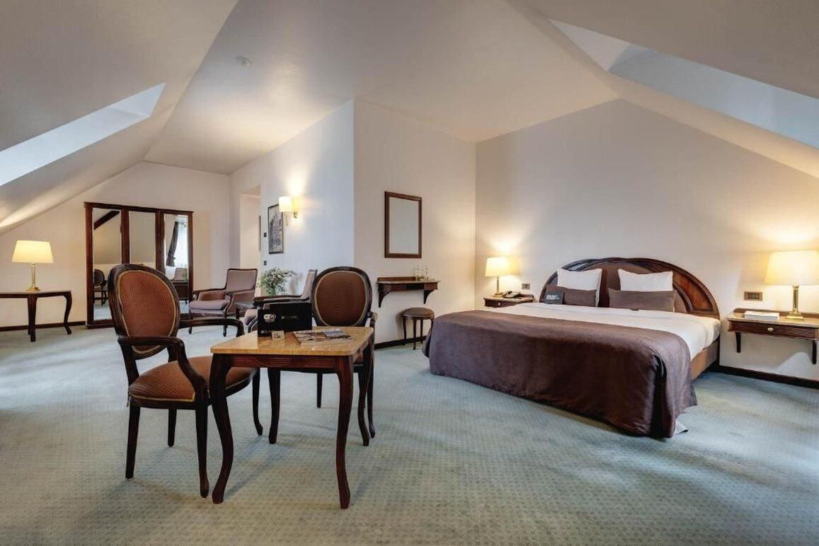 Une chambre d’hôtel avec un grand lit, un bureau avec deux chaises, une petite table et un miroir.