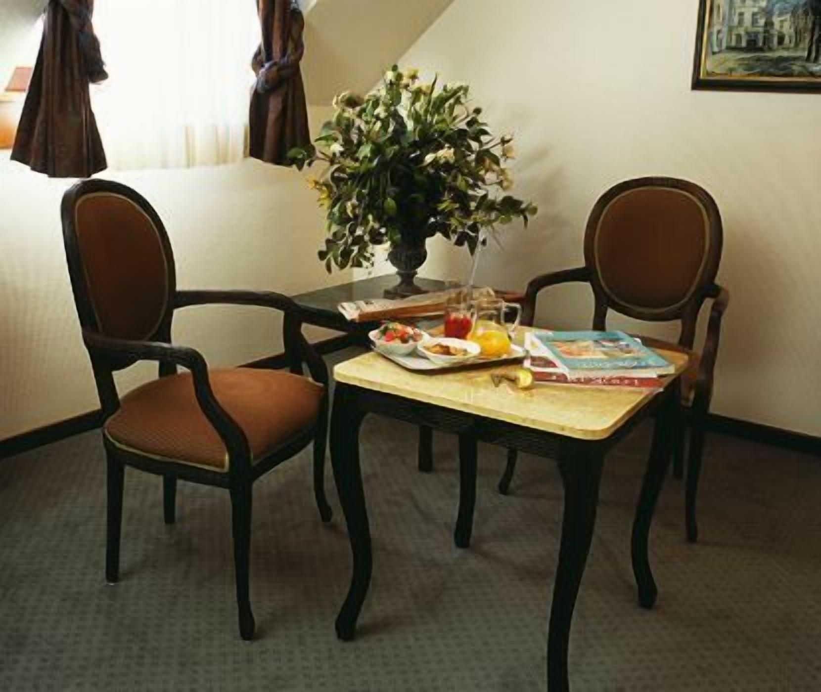 A dining area with two chairs, a table, and a vase with flowers.