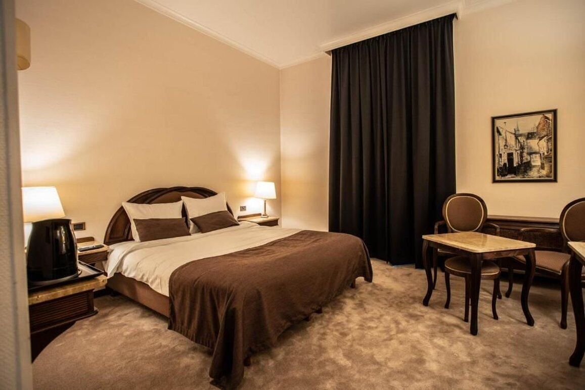 A hotel room with a large bed, two bedside tables with lamps, a desk with chairs, and a painting on the wall.