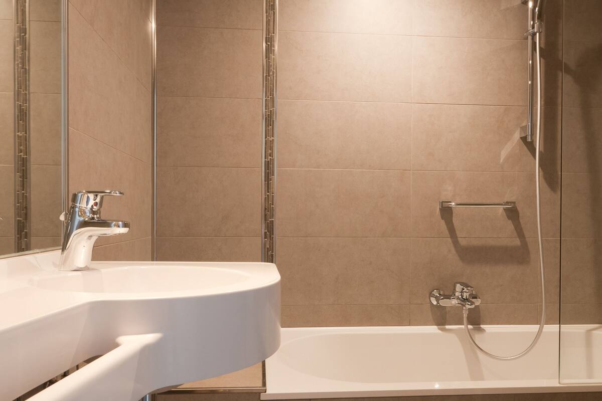 A modern bathroom with a white sink, a glass-enclosed shower, and beige tiled walls.