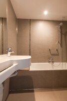 A modern bathroom with a white sink, a glass-enclosed shower, and beige tiled walls.