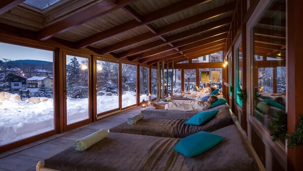 A cozy cabin with large windows, wooden beams, and a view of a snowy landscape.
