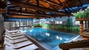 An indoor swimming pool with wooden beams, a mural of a mountainous landscape, and lounge chairs.