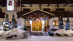 A hotel entrance with a snow-covered driveway, a wooden bench, and Christmas trees.