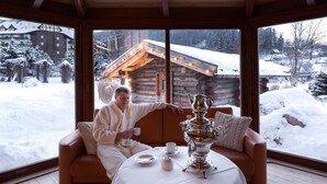 A cozy room with a large window, a wooden ceiling, and a view of a snowy landscape and a cabin.