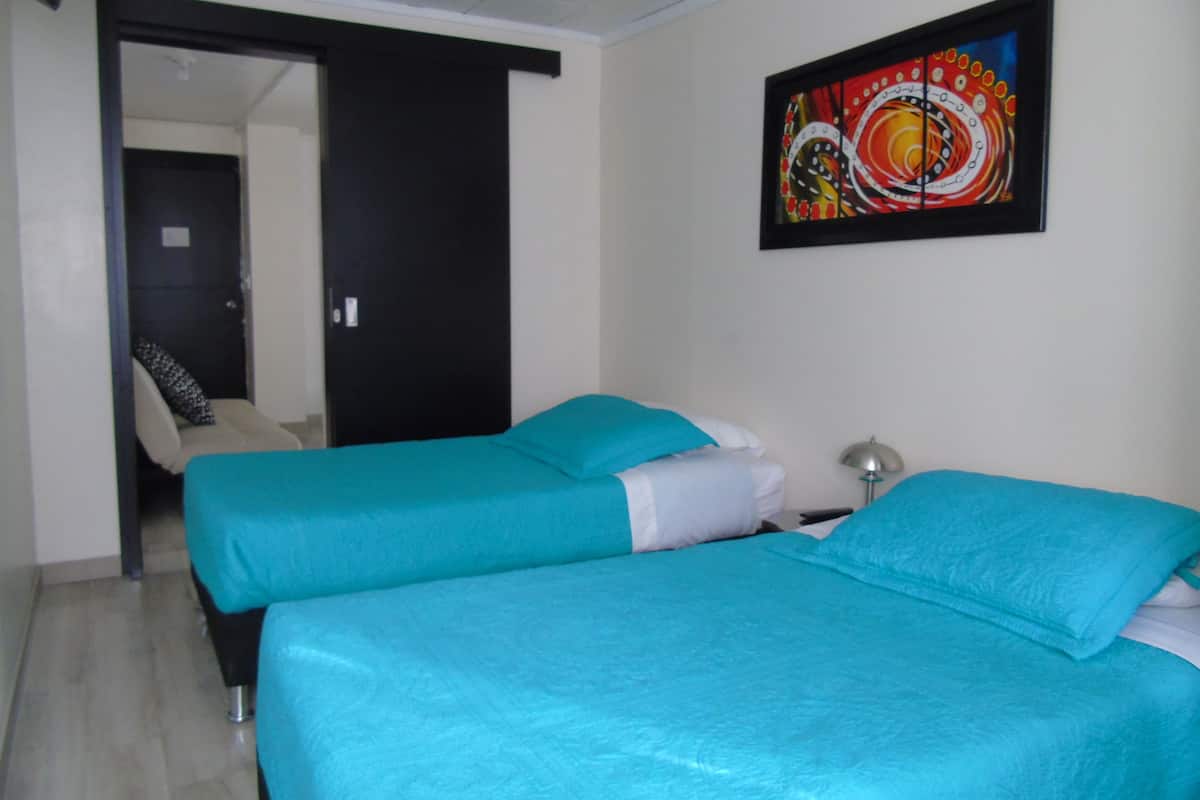 A room with two beds, a door, a chair, and a painting on the wall.