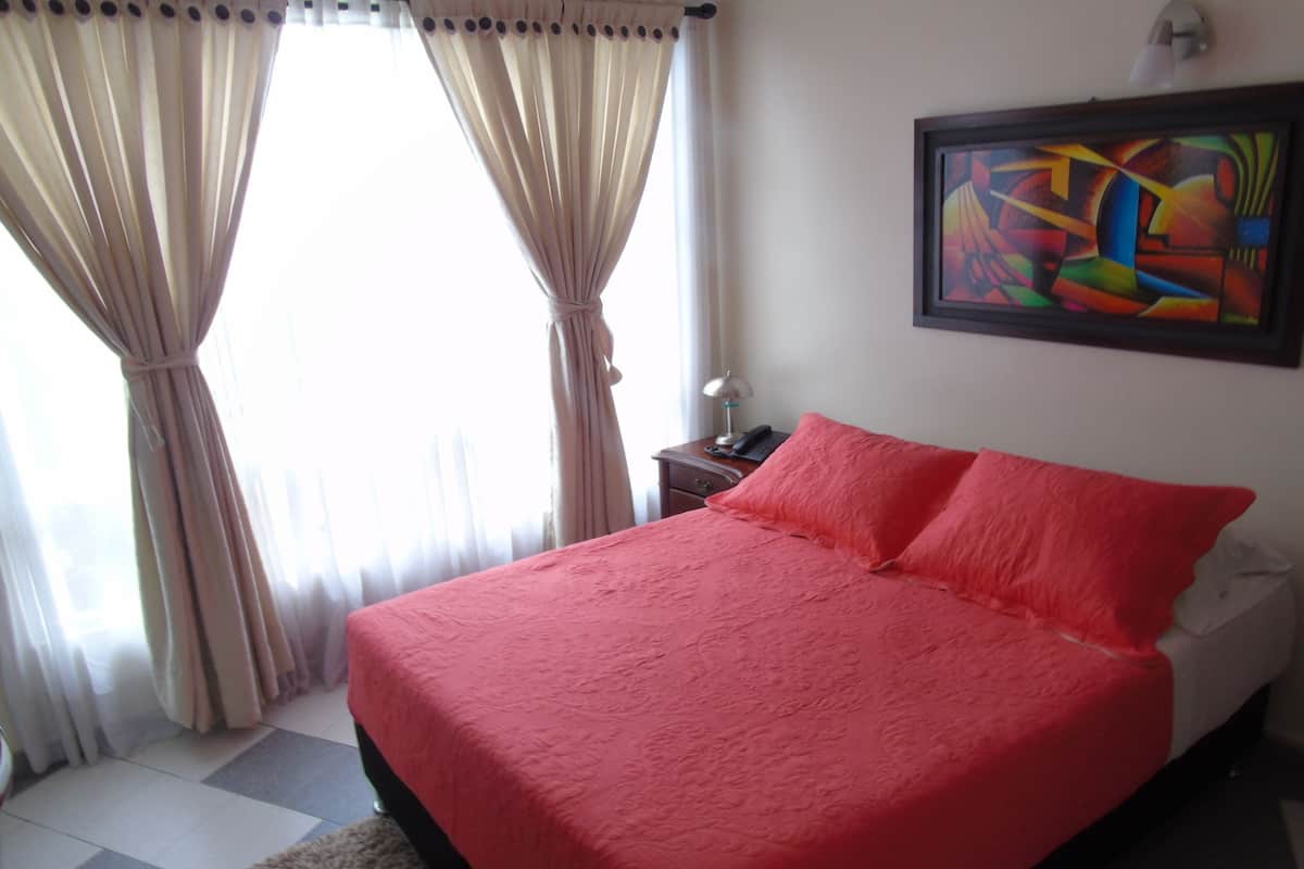 A bedroom with a large bed, a nightstand, a lamp, and a painting on the wall.