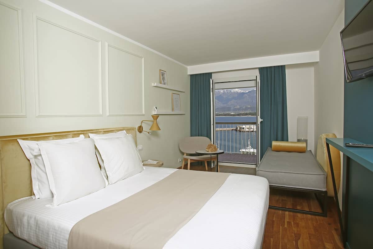 Habitación de hotel con una cama grande, una cama más pequeña, una silla, una mesa y vista al mar.