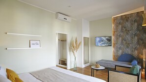 A modern hotel room with a large bed, a seating area with a sofa and armchair, a small table, and a wall-mounted TV. - Hotel Balanea (Calvi)