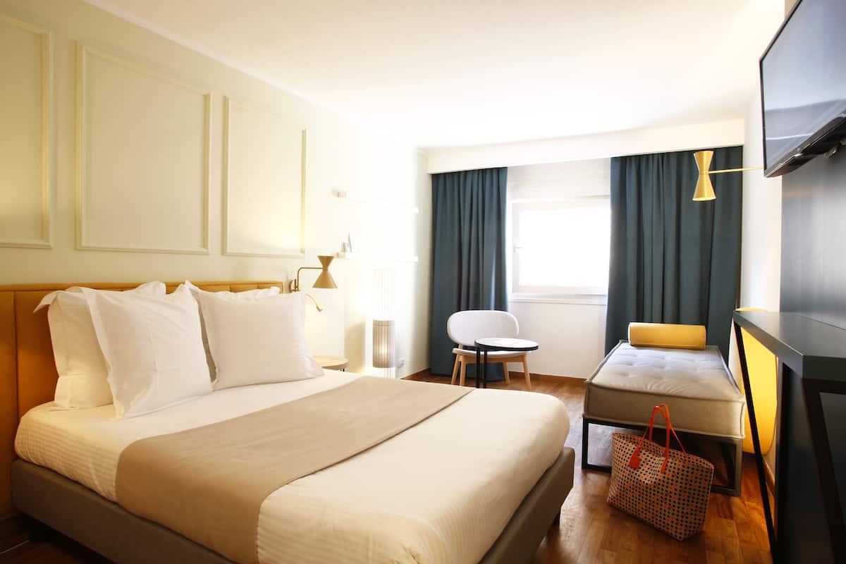 Habitación de hotel con una cama grande, un sofá pequeño, una silla, un televisor y una lámpara.