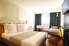 Habitació d'hotel amb un llit gran, un sofà petit, una cadira, un televisor i una làmpada.