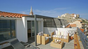 A rooftop terrace with wicker furniture, a glass balustrade, and a view of historic buildings in the background. - Hotel Balanea (Calvi)