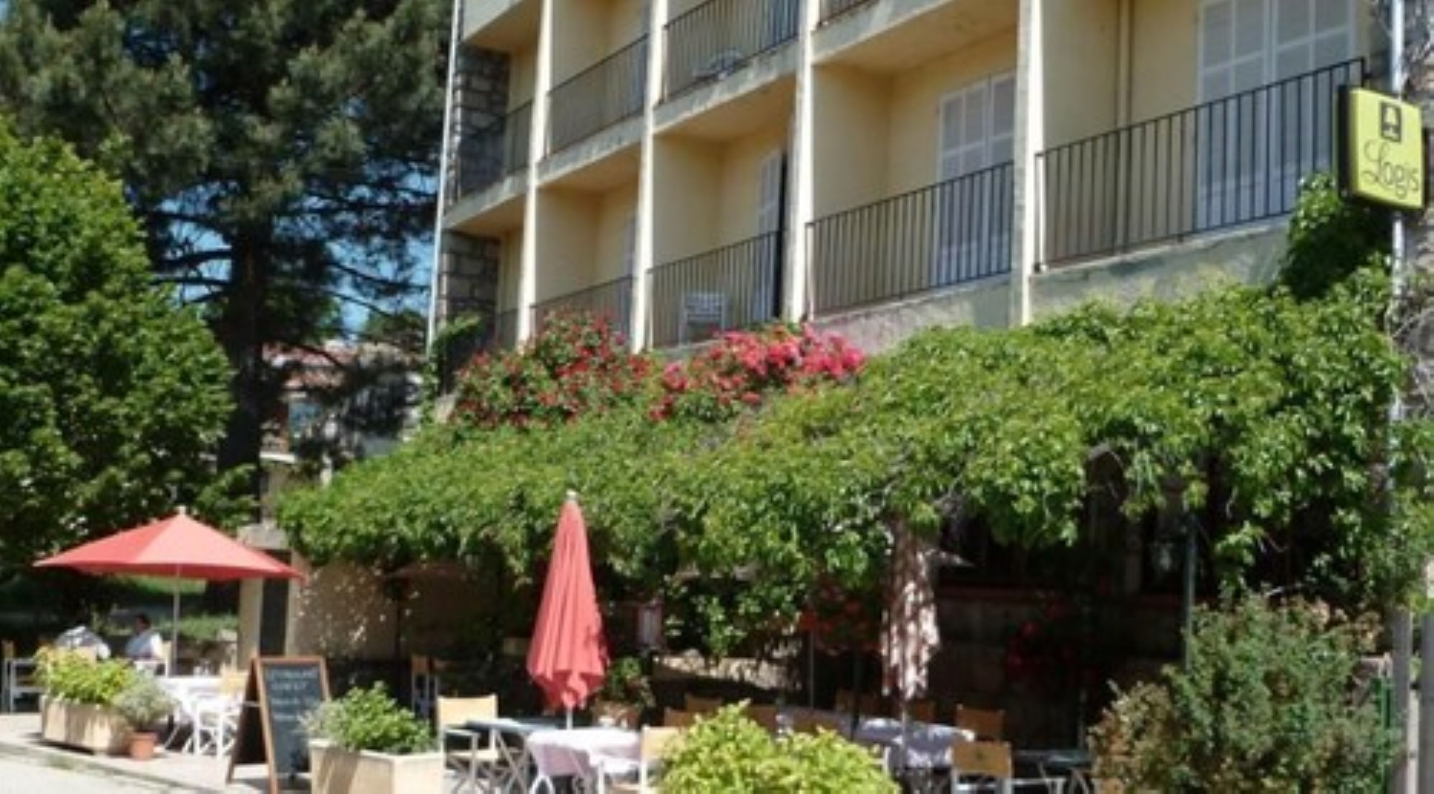 Un edificio de varios pisos con balcones, mobiliario exterior y un jardín con flores rojas.