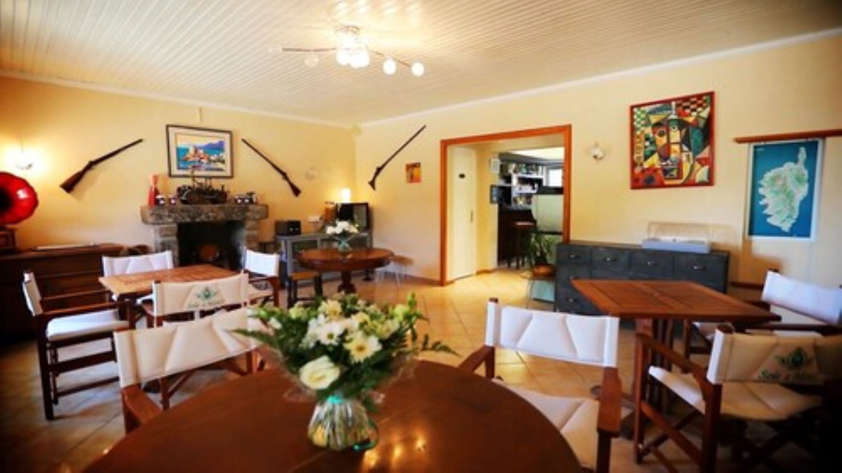 A dining area with a round table, chairs, and a vase of flowers. There is a fireplace with a mantel and a painting on the wall.