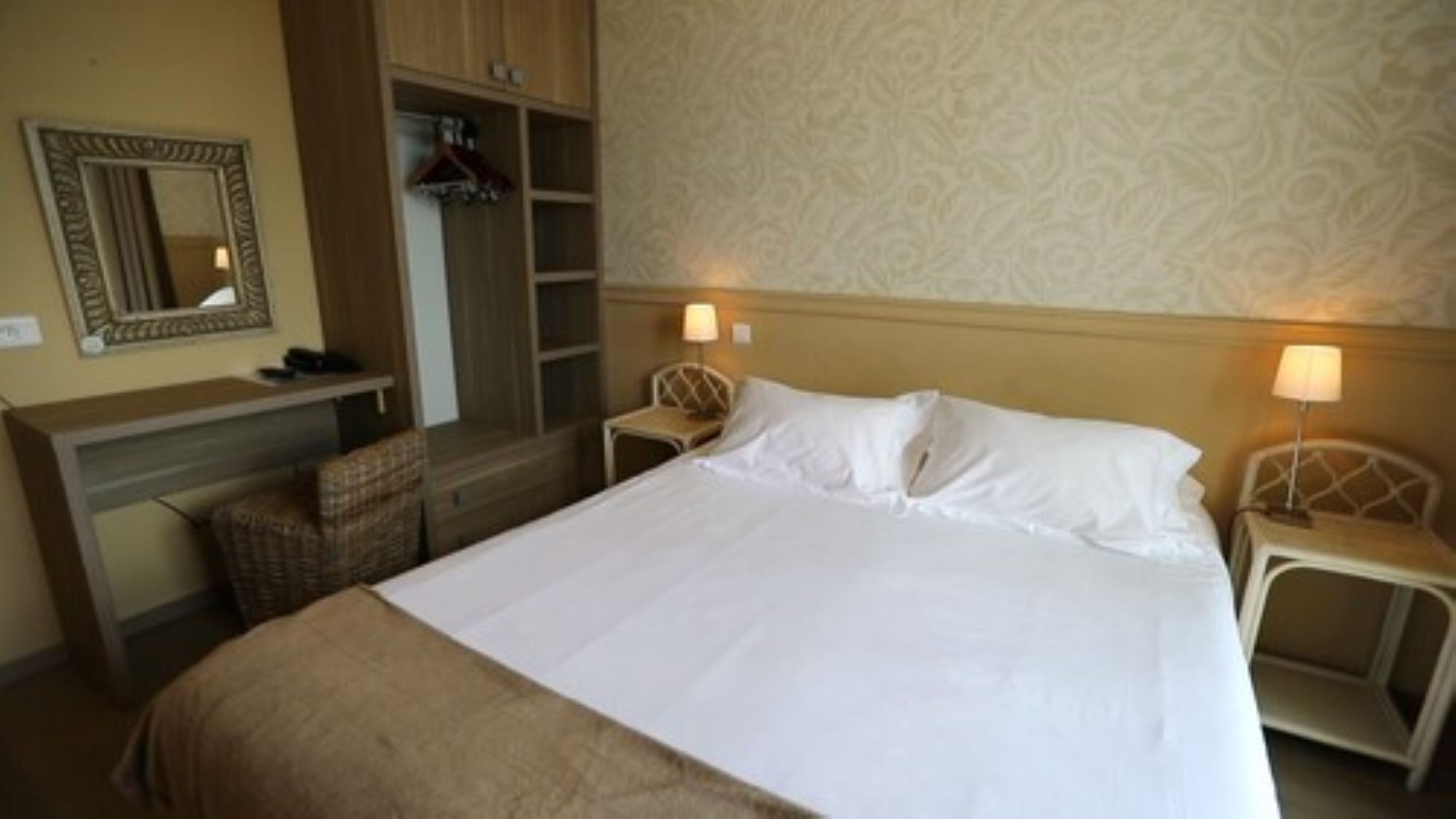 Habitación de hotel con una cama grande, un escritorio con una silla, un armario y dos lámparas de noche.