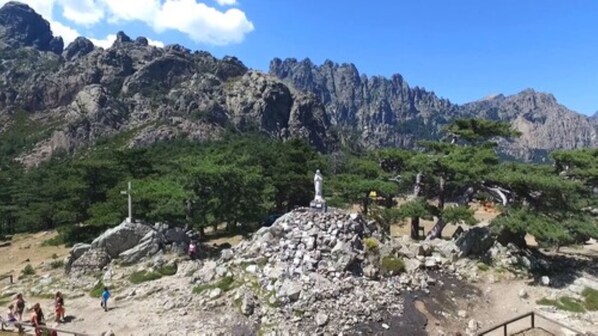 Terreno rocoso con una estatua en una colina, rodeado de árboles y montañas.