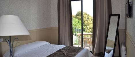 Habitación de hotel con cama, lámpara, espejo y vista a un balcón con vegetación.