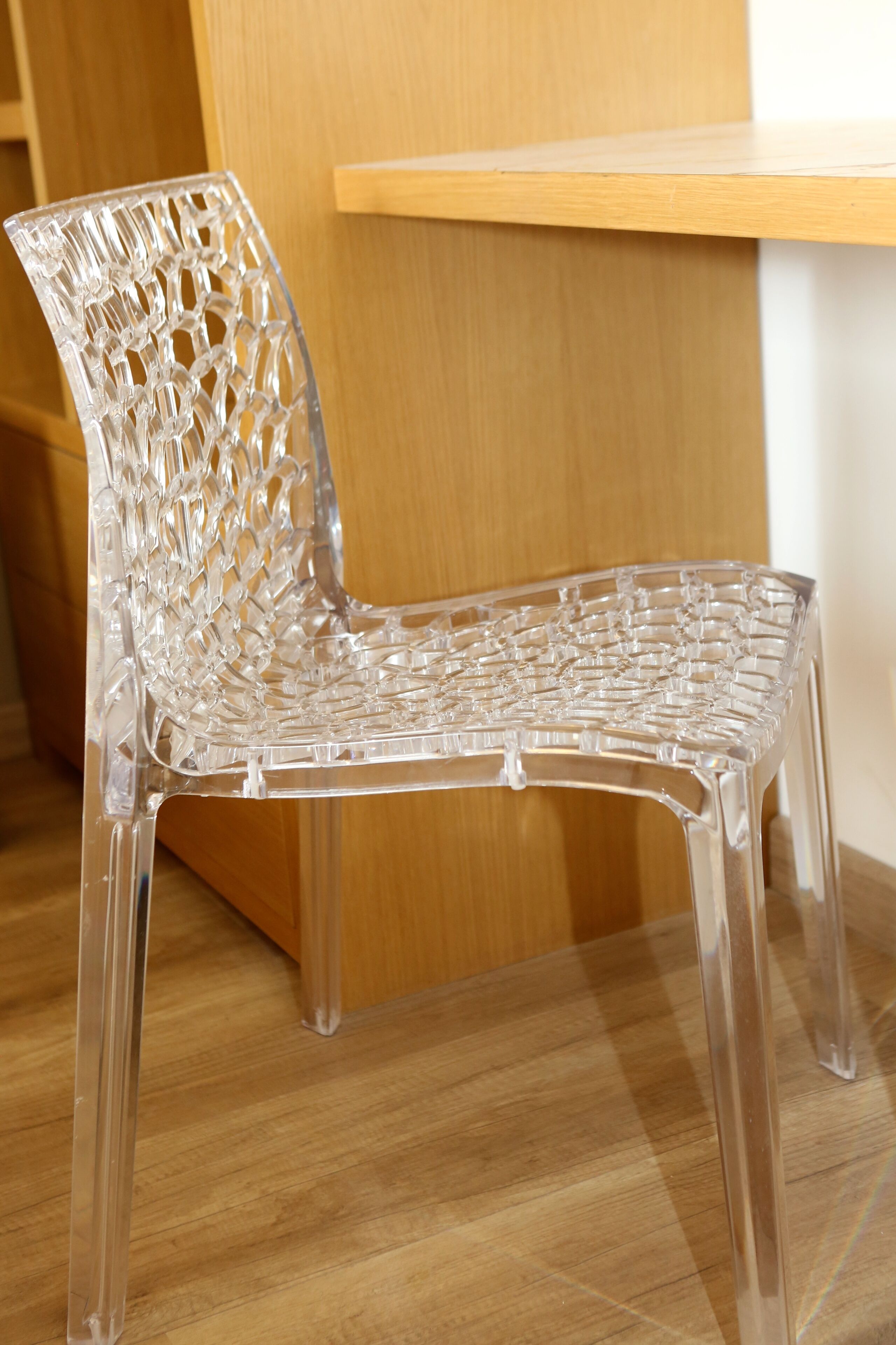 Une chaise en plastique transparent ornée d’un motif géométrique, posée sur un plancher en bois.