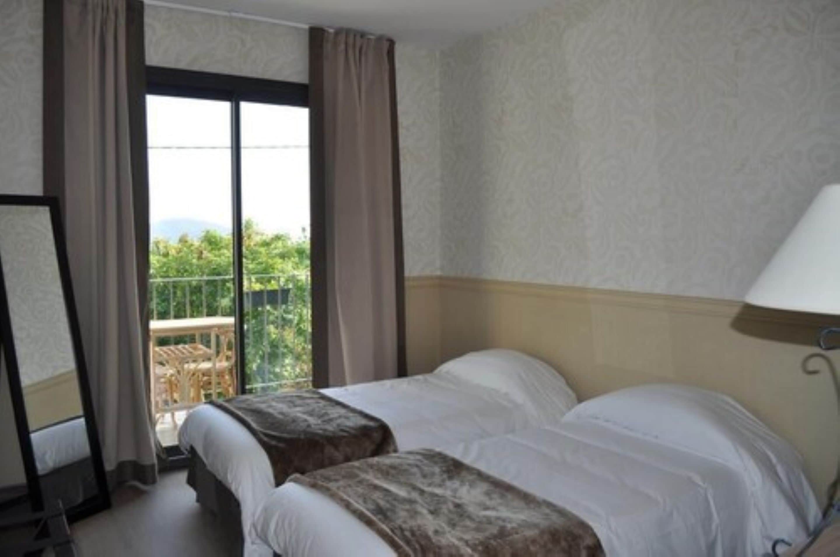 A hotel room with two beds, a balcony with a view, and a large window.