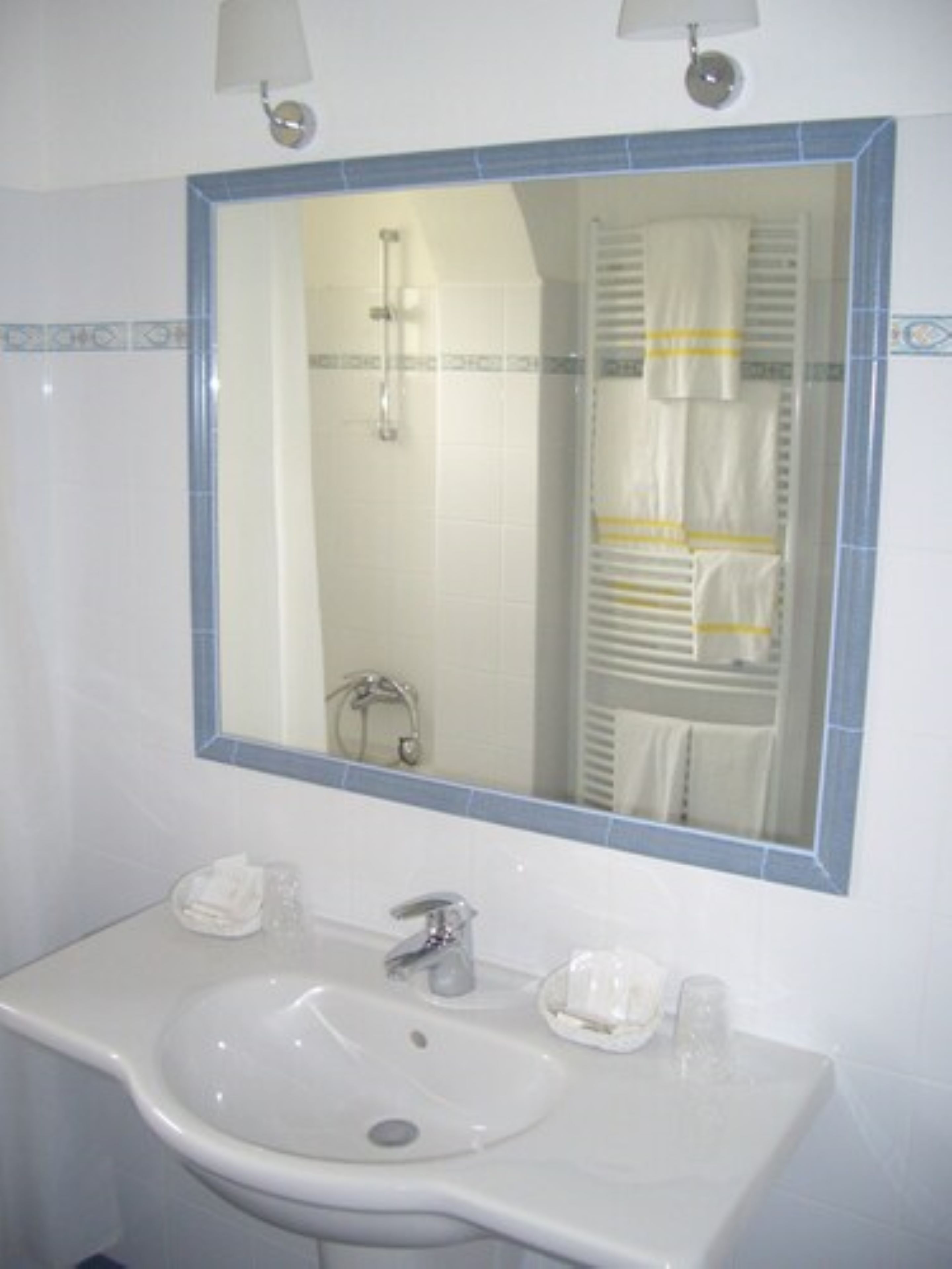 Un baño con un lavamanos blanco, un espejo y un perchero para toallas.
