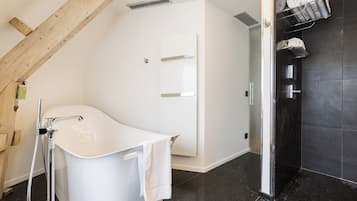 A modern bathroom with a freestanding bathtub, a shower area, and a towel rack with neatly rolled towels.