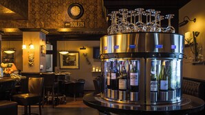 Un espace bar doté d’un distributeur de boissons en acier inoxydable, de verres à vin disposés sur le comptoir, et d’un panneau indiquant la direction des toilettes.