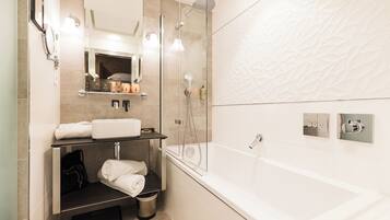 A modern bathroom with a glass-enclosed shower, a large white bathtub, and a vanity with a mirror and towel rack.