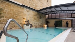 Une piscine équipée d’une rampe métallique, une horloge au mur et un espace abrité avec un toit en verre.