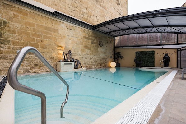 A swimming pool with a metal handrail, a clock on the wall, and a covered area with a glass roof.