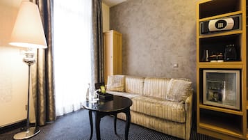 A hotel room with a sofa, a table, a lamp, a cabinet with a microwave, and a bookshelf.