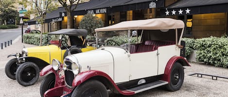 A vintage car parked in front of a building with a black awning and a sign that reads "Plaza Madeline."