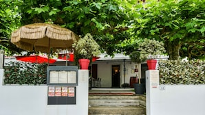 A hotel entrance with steps leading up to the door, a thatched umbrella, and potted plants. - Auberge L'Estanquet (Urt)